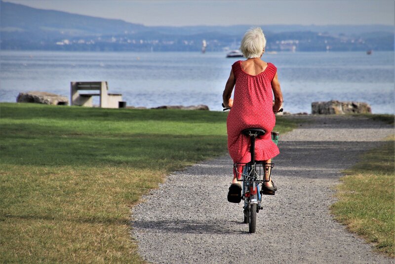 Senior woman going for a leisurely bike ride by the water on a sunny day: massage is for everyone and helps achieve health goals